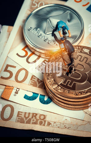 macro miner figurines working on stack of bitcoin and ethereum placed on euro banknotes. virtual crypto currency mining and trading concept Stock Photo