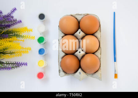 Easter brown chicken eggs in carton container, with paints, colorful palette, paint equipment on white background Stock Photo