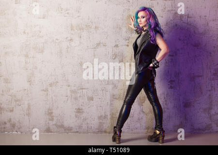 Daring rebel rocker, a portrait on a background of gray grunge wall. Young stylish woman in black leather clothes with colored hair. Bright hair color. Stock Photo