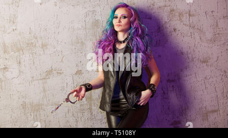 Daring rebel rocker, a portrait on a background of gray grunge wall. Young stylish woman in black leather clothes with colored hair. Bright hair color. Stock Photo