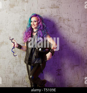 Daring rebel rocker, a portrait on a background of gray grunge wall. Young stylish woman in black leather clothes with colored hair. Bright hair color. Stock Photo