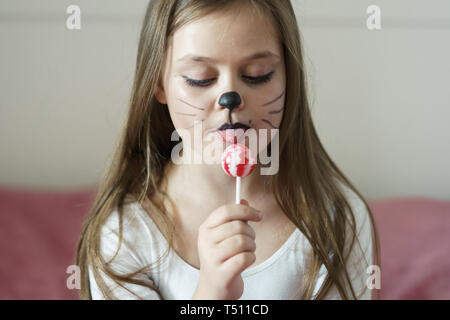 blonde girl with a make-up imitating a cat holds in her hand a chupa chups. Stock Photo