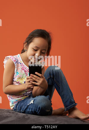 Asian girl playing with phone on a beanbag and a background color. Stock Photo