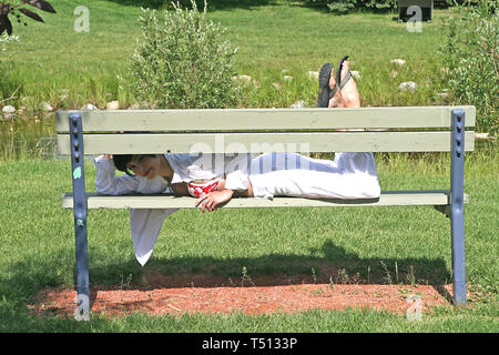 Pretty dark haired woman lying on a wooden  park bench. Stock Photo