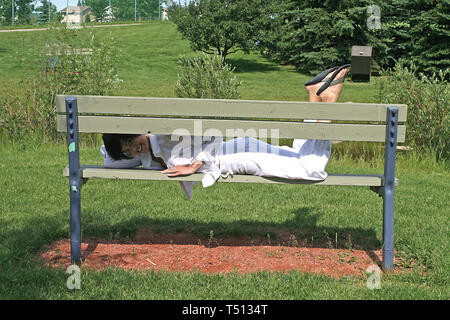 Pretty dark haired woman lying on a wooden  park bench. Stock Photo