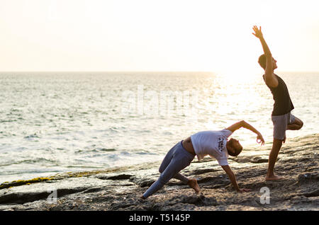 Two friends practicing Yoga on the edge of the ocean at sunset, Yoga or meditation concept Stock Photo