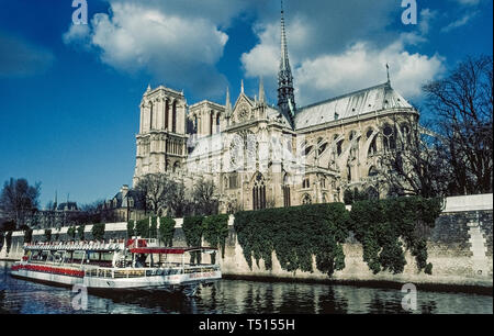 An excursion boat on the River Seine passes by the gothic Notre-Dame de Paris, the famous Catholic cathedral in the French capital that is one of Europe's most popular tourist attractions. This photograph was taken before the historic church suffered major damage by a disastrous fire in April, 2019, and was closed for restoration. Construction of the ancient stone structure began in the 12th Century and featured ornate medieval architecture that included twin bell towers, stained-glass rose windows, flying support buttresses and the soaring wooden central spire (that was destroyed in the fire) Stock Photo