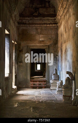 Broken statues sit in a sandstone hallway illuminated by sunlight in Angkor Wat, Angkor Archaeological Park, Cambodia. Stock Photo
