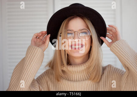 charming young woman in a soft sweater and glasses, in a black felt hat. Portrait of a happy smiling girl in stylish glasses Stock Photo