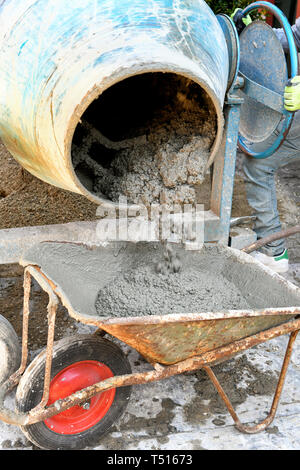 The technician worker loading cement into wheelbarrow pouring it out of electric concrete mixer for construction works Stock Photo
