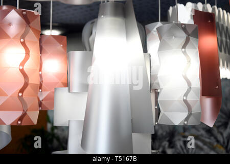 Modern design plastic chandeliers of matte white and light red colors with glowing lamps, viewed in close-up Stock Photo
