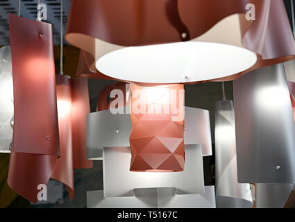 Modern plastic chandeliers of red and silver colors with geometrical shape design and glowing lamps, hanging on white wires. Viewed in close-up from l Stock Photo