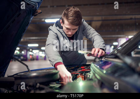 Man with phone in hand mending broken car with open hood in underground parking Stock Photo