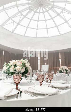 Flower arrangement in the center of the table. Interior of restaurant for wedding dinner, ready for guests. Round Banquet table served. Catering Stock Photo