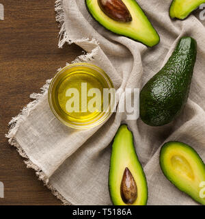 Sliced and whole avocadoes and bowl of oil on table Stock Photo