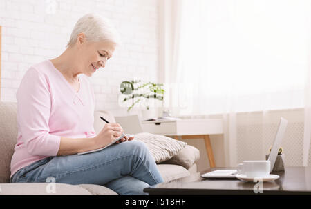 Senior woman rewriting recipe from laptop to notebook Stock Photo