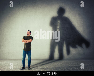 Casual man, keeps arms crossed smiling confident, casting a superhero with cape shadow on the wall. Ambition and business success concept. Leadership  Stock Photo