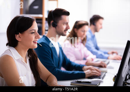 Happy Young Customer Service Executives Using Earphones Working In Call Center Stock Photo