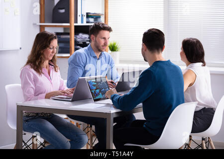 Side View Of Businesspeople Analyzing Graph On Laptop At Workplace In The Office Stock Photo