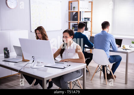 Smiling Young Businesspeople Using Electronic Devices At Workplace In Office Stock Photo