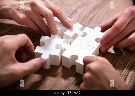 Close-up Of Businesspeople Solving White Jigsaw Puzzle Together On Wooden Desk Stock Photo