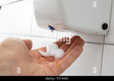 Close-up Of Person's Hand With Liquid Soap Dispenser On Tiled Wall Stock Photo