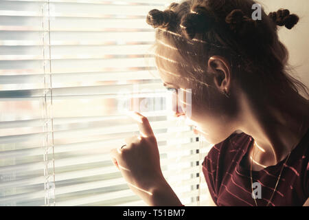 sad woman looking through blinds on window Stock Photo