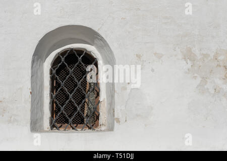 Old white stone wall with one arched grating window Stock Photo
