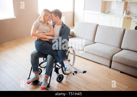 Young man with disability and special needs holding girlfriend on knees. They lean to each other and smile. Lovely couple happy together Stock Photo