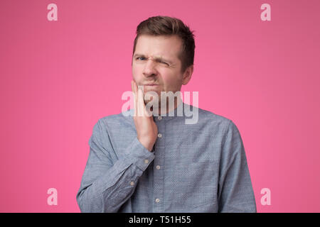 Young caucasian man is having toothache holding his cheek. Stock Photo