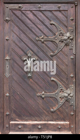 Ancient antique wooden doors with wrought iron loops, massive forged door handle and cross bars. Stock Photo