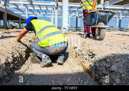 Mason is using a trowel to align first level of the concrete foundation in trench. Stock Photo