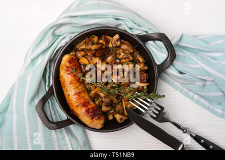Cast-iron pan with fried sausage and mushrooms, flat lay, top view. Stock Photo