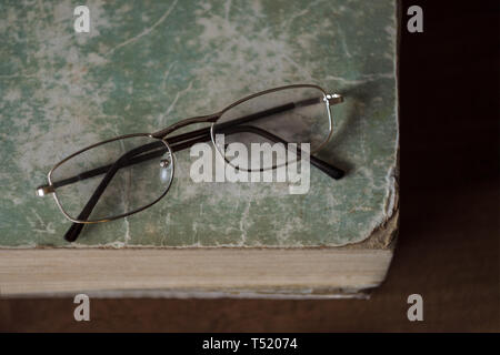 Glasses lie on an old book with torn edges with a shabby cover. The concept of learning, reading and education. Top view. Stock Photo