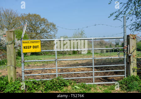 A yellow sign instructing visitors to keep out of private property is attached to a metal gate in South Staffordshire countryside near Perton village. Stock Photo