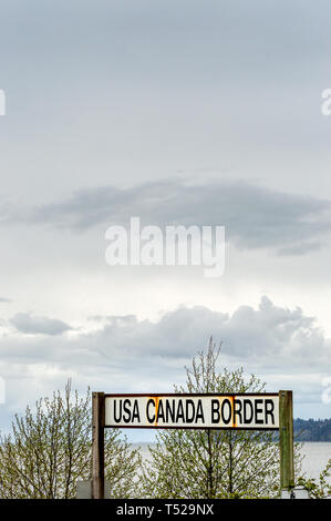 April 14, 2019 - Surrey, British Columbia: BNRR Railway USA Canada border sign and Semiamoo Bay to the West under overcast sky. Stock Photo