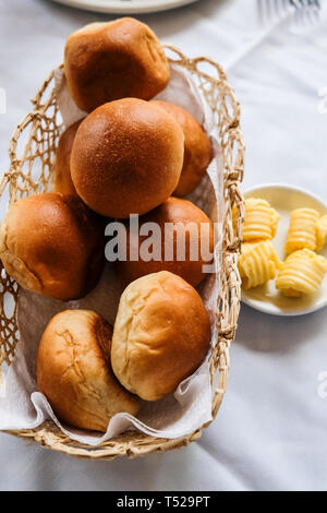 Close up of freshly baked bread rolls in basket and butter in small plate on dinning table Stock Photo