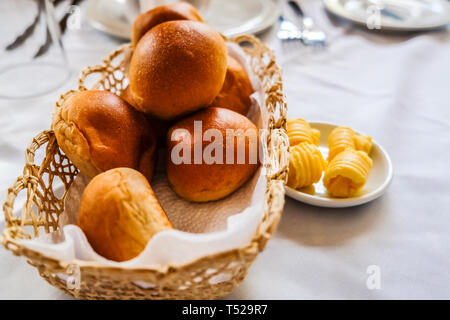 Close up of freshly baked bread rolls in basket and butter in small plate on dinning table Stock Photo