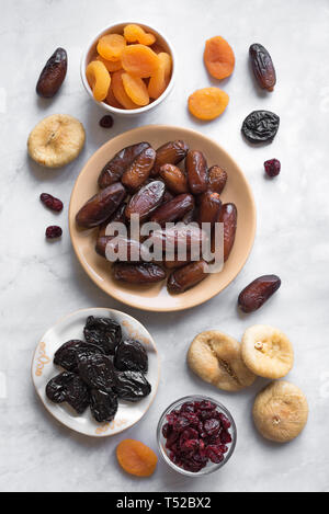 Dried fruits in bowls on white marble background, top view. Healthy snack - assortment of organic dry fruits. Stock Photo