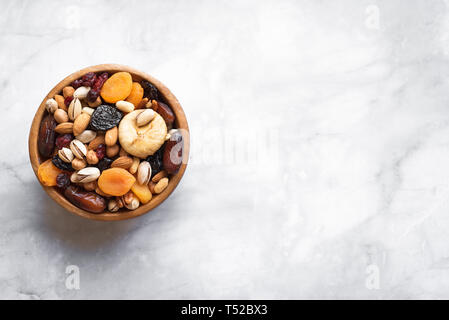 Mixed nuts and dried fruits in wooden bowl on white marble background, copy space. Healthy snack - mix of organic nuts and dry fruits. Stock Photo