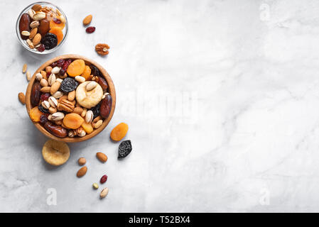 Mixed nuts and dried fruits in wooden bowl on white marble background, copy space. Healthy snack - mix of organic nuts and dry fruits. Stock Photo