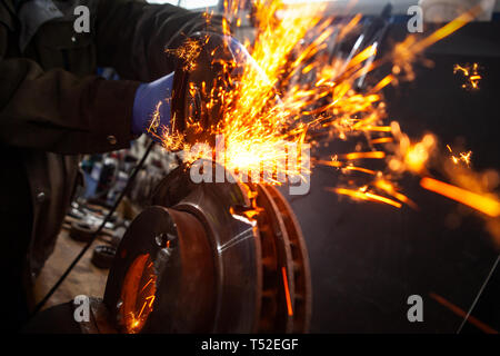 Close-up of a man sawing   bearing metal brake disk with a hand circular saw, bright flashes flying in different directions, in the background tools f Stock Photo