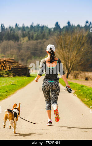 Girl running with dog outdoors in nature on a road to forest. Sunny day countryside sunset. Stock Photo