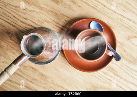 Coffee in oriental Turkish style served in cezve, a small long-handled pot with a pouring lip and cup on a wooden table Stock Photo