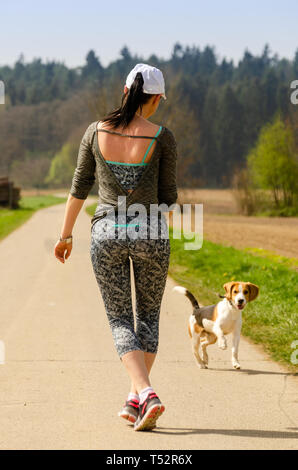 Girl running with dog outdoors in nature on a road to forest. Sunny day countryside sunset. Stock Photo