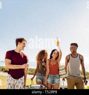 Group of men and women at walking outdoors with beers. Friends having a great time together. Young people going on picnic on a summer day. Stock Photo