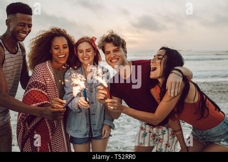 Happy friends partying on the beach with sparklers. Multi-ethnic group of friends together at the beach celebrating with fireworks. Stock Photo