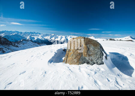 Panoramic view down snow covered valley in alpine mountain range on blue sky background with rock in foreground Stock Photo