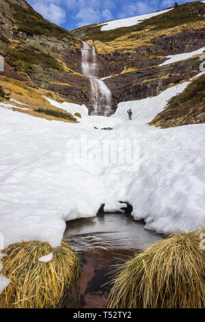 Low angle view of mountain hiker taking a photo with a mobile phone of the large, scenic, beautiful waterfall falling from red rocky cliff under the s Stock Photo