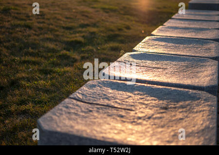 Bench of granite on a background of green grass in the rays of sunset Stock Photo